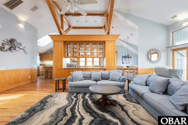 living area with lofted ceiling with skylight, light wood-type flooring, wainscoting, and visible vents