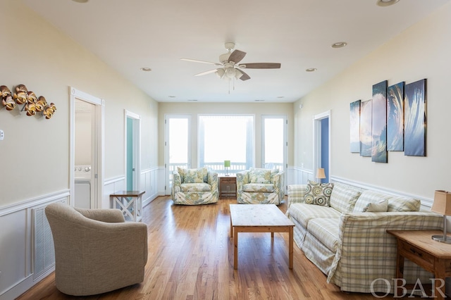 living room featuring a wainscoted wall, light wood-style flooring, and ceiling fan