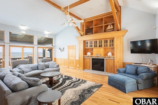 living area featuring a water view, wood finished floors, wainscoting, beamed ceiling, and a glass covered fireplace