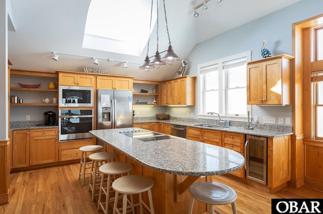 kitchen with light wood finished floors, wine cooler, appliances with stainless steel finishes, a breakfast bar area, and a sink