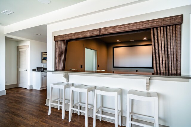 kitchen with baseboards, visible vents, white cabinets, dark wood-style floors, and a breakfast bar