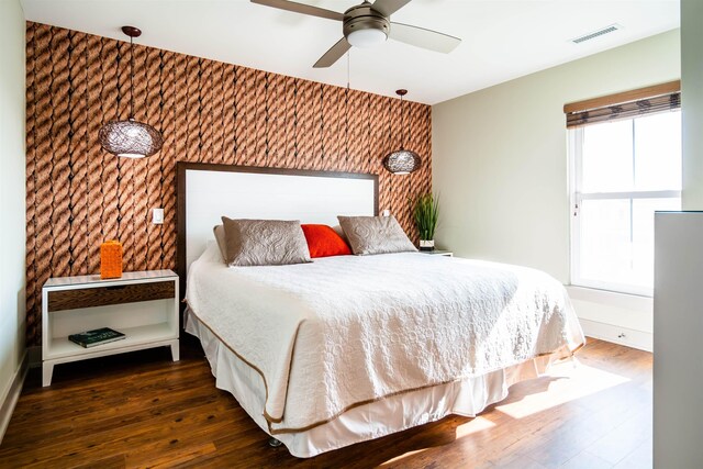 bedroom with an accent wall, visible vents, dark wood finished floors, and wallpapered walls