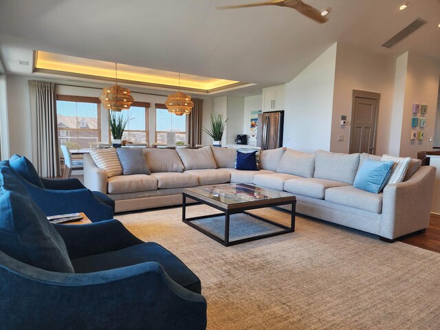 living room featuring visible vents, a tray ceiling, and light wood-style flooring