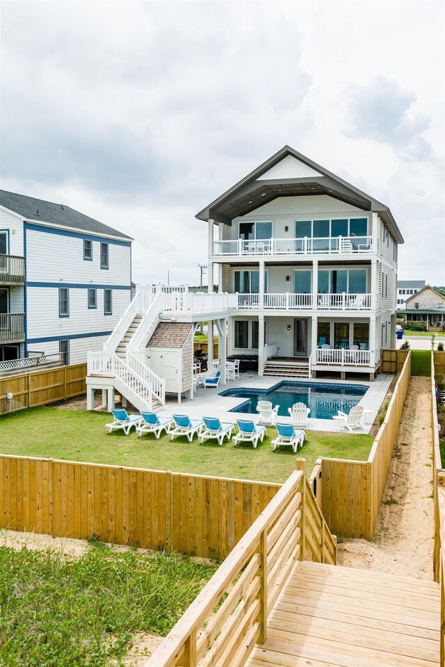 back of house featuring stairway, a patio area, a balcony, a fenced backyard, and an outdoor pool