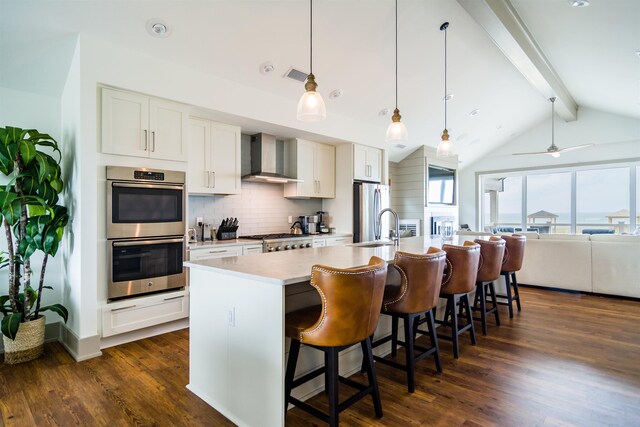 kitchen featuring white cabinetry, light countertops, appliances with stainless steel finishes, wall chimney exhaust hood, and a center island with sink