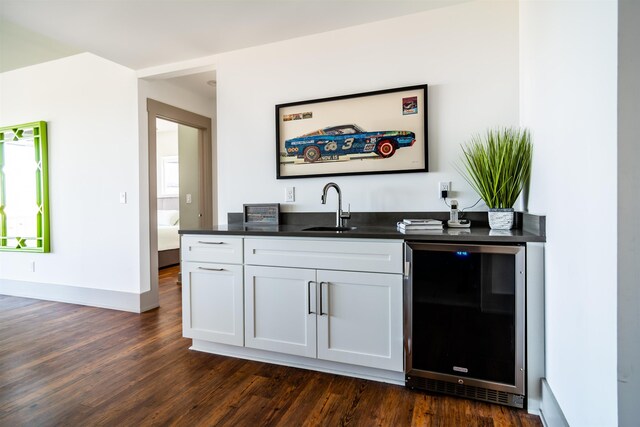 bar featuring dark wood-style floors, indoor wet bar, a sink, beverage cooler, and baseboards