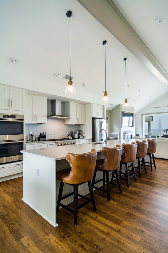 kitchen with stainless steel appliances, light countertops, a large island with sink, and wall chimney exhaust hood