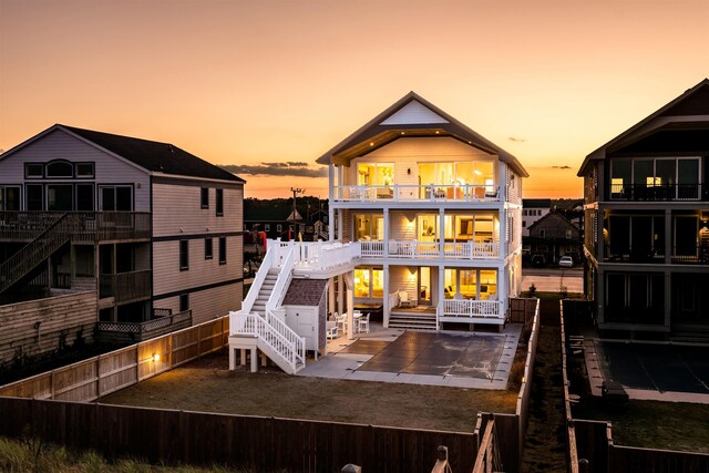 back of house at dusk with a balcony, a fenced backyard, stairway, and a patio