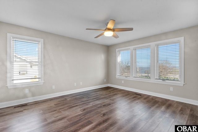 unfurnished room with a wealth of natural light, visible vents, and dark wood finished floors