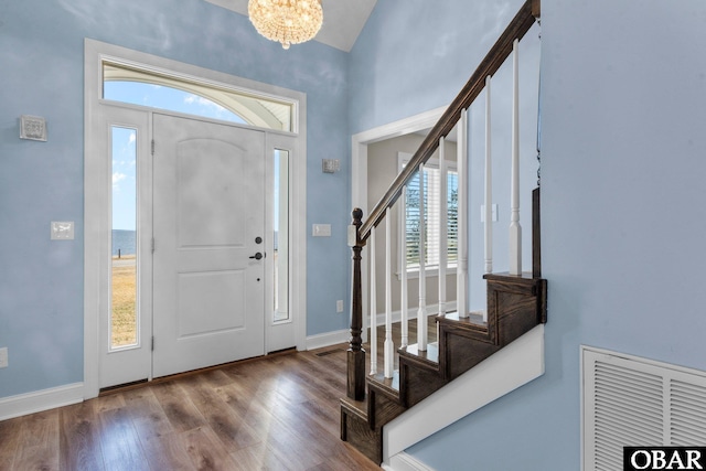 foyer entrance with wood finished floors, visible vents, baseboards, stairway, and an inviting chandelier