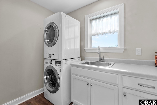 clothes washing area with stacked washer and dryer, cabinet space, dark wood-type flooring, a sink, and baseboards