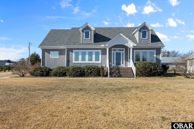 new england style home featuring a shingled roof and a front yard