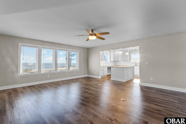 unfurnished living room with visible vents, dark wood-type flooring, a ceiling fan, a sink, and baseboards