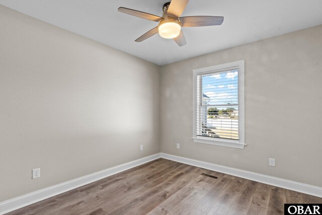 empty room featuring ceiling fan, visible vents, baseboards, and wood finished floors