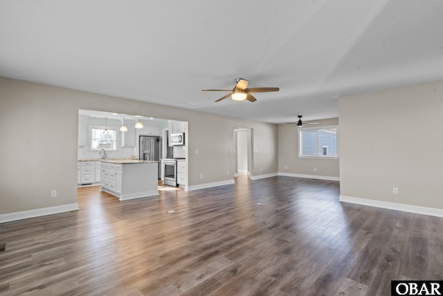 unfurnished living room with dark wood-type flooring, a sink, a ceiling fan, and baseboards