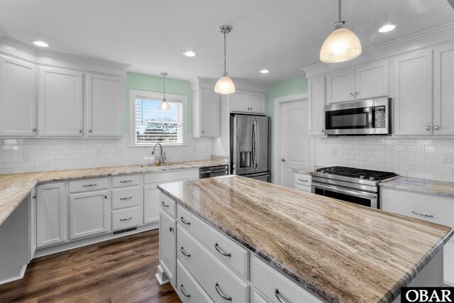 kitchen with hanging light fixtures, appliances with stainless steel finishes, white cabinets, and a sink