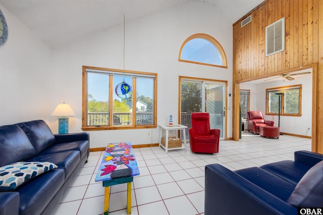 living area with light tile patterned flooring, visible vents, wood walls, and high vaulted ceiling