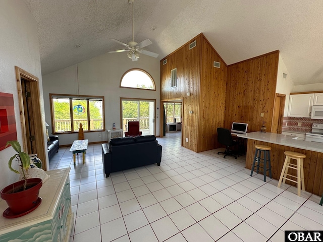 living area with light tile patterned flooring, visible vents, wood walls, and high vaulted ceiling