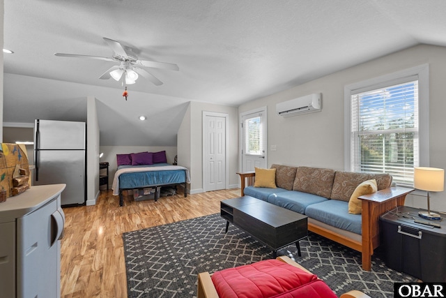 living area with an AC wall unit, a ceiling fan, vaulted ceiling, and light wood-type flooring