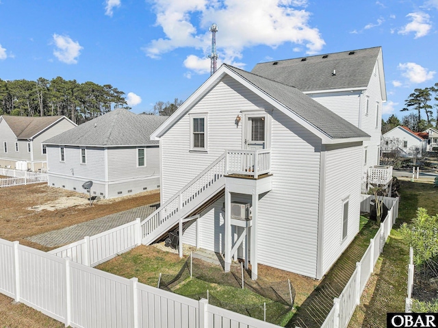 rear view of property featuring a fenced backyard, stairway, and a shingled roof