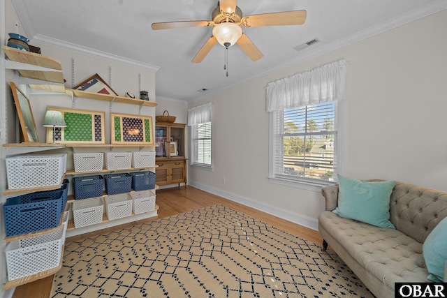 interior space with a ceiling fan, visible vents, wood finished floors, baseboards, and ornamental molding
