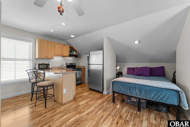 kitchen with appliances with stainless steel finishes, a breakfast bar, light brown cabinets, baseboards, and lofted ceiling