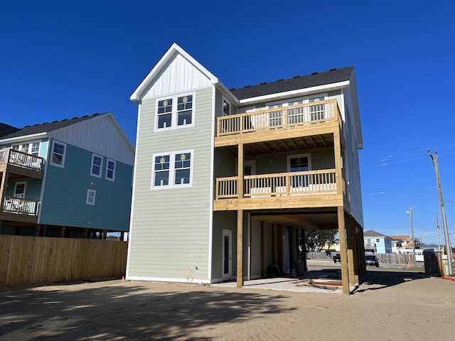 back of house featuring driveway, board and batten siding, a balcony, fence, and a carport