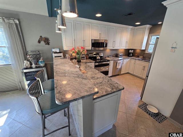 kitchen featuring stone counters, stainless steel appliances, white cabinets, a peninsula, and a kitchen breakfast bar