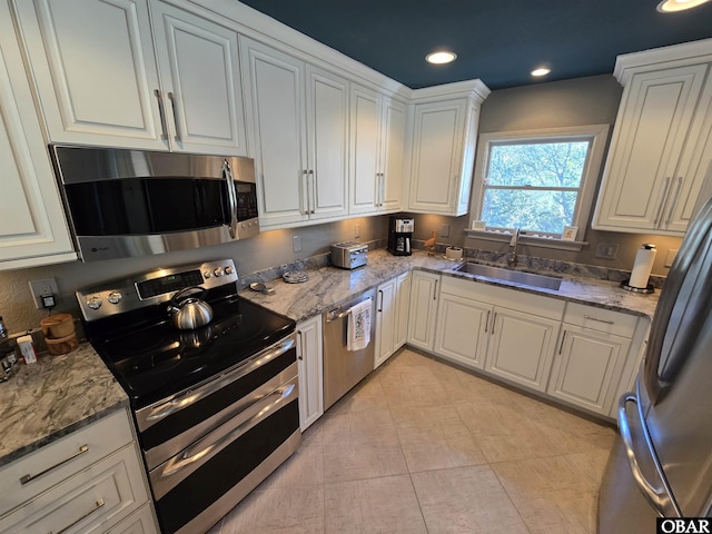 kitchen featuring stainless steel appliances, white cabinetry, a sink, and light stone countertops