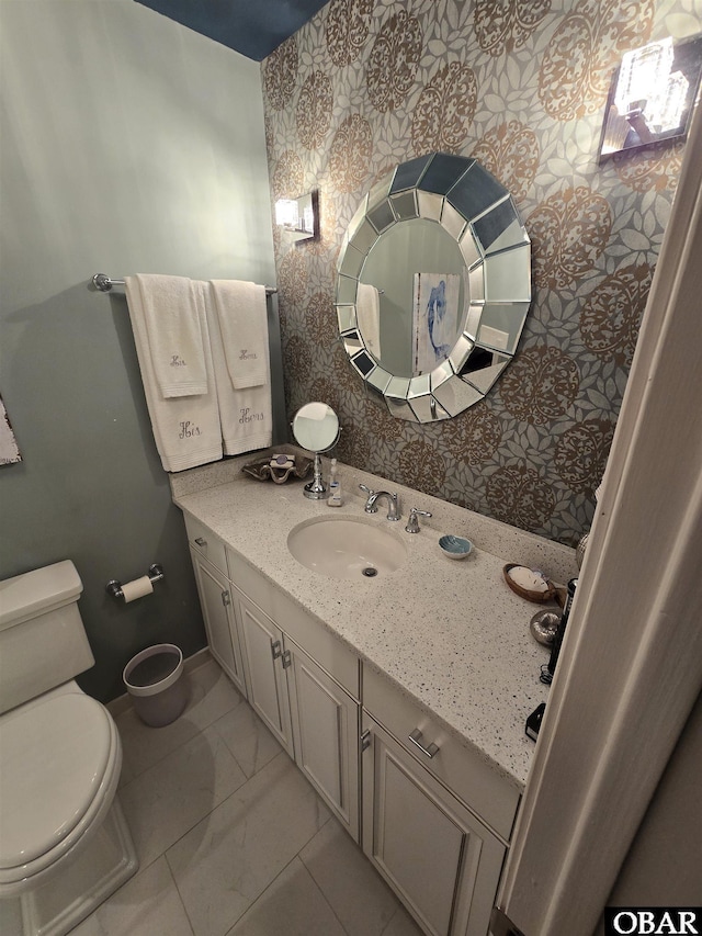 bathroom with baseboards, vanity, toilet, and wallpapered walls