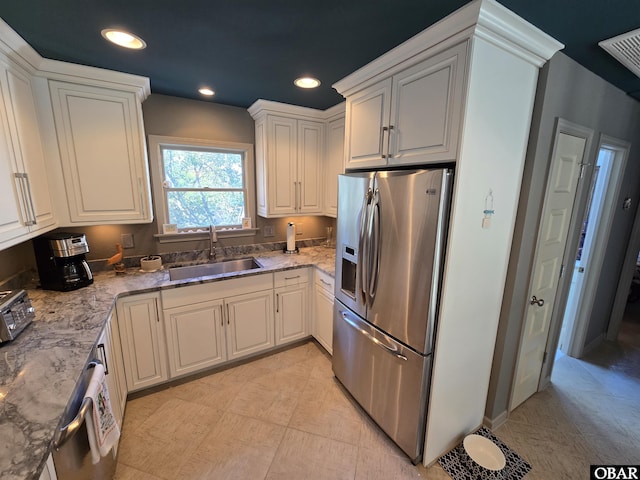 kitchen featuring stainless steel fridge, white cabinets, light stone countertops, a sink, and recessed lighting