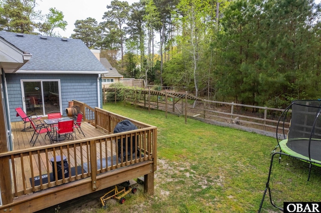 view of yard featuring a trampoline, a deck, fence private yard, and outdoor dining area