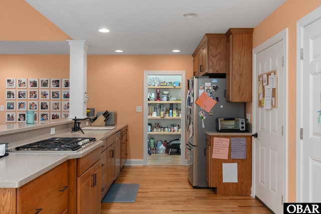 kitchen featuring light wood-style flooring, appliances with stainless steel finishes, a sink, light countertops, and brown cabinets