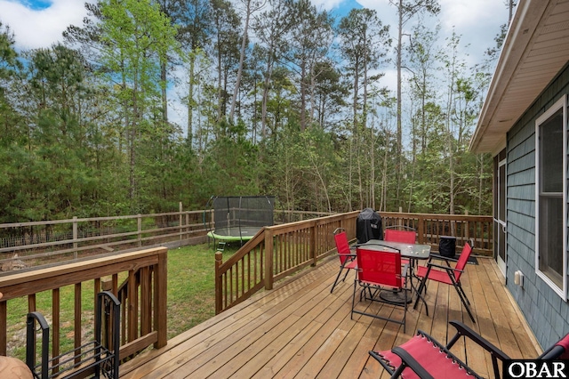 deck with a lawn, a trampoline, a fenced backyard, and outdoor dining space