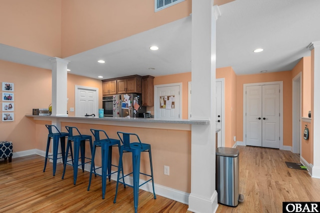 kitchen featuring visible vents, freestanding refrigerator, light wood-type flooring, a kitchen breakfast bar, and ornate columns