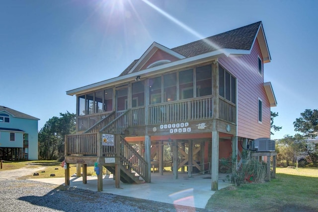 view of front facade featuring central AC unit, a sunroom, stairs, roof with shingles, and a patio area