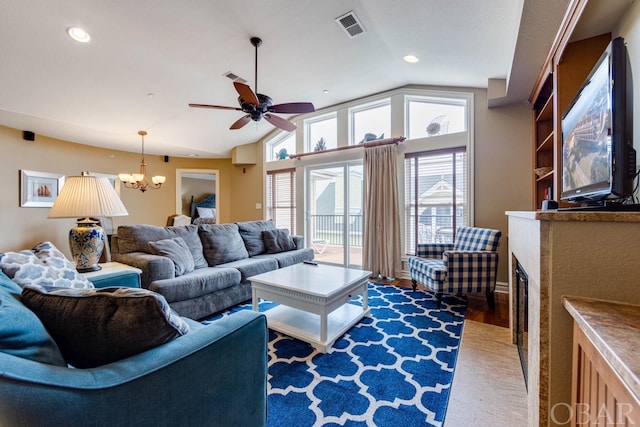 living area with a fireplace, visible vents, vaulted ceiling, wood finished floors, and ceiling fan with notable chandelier