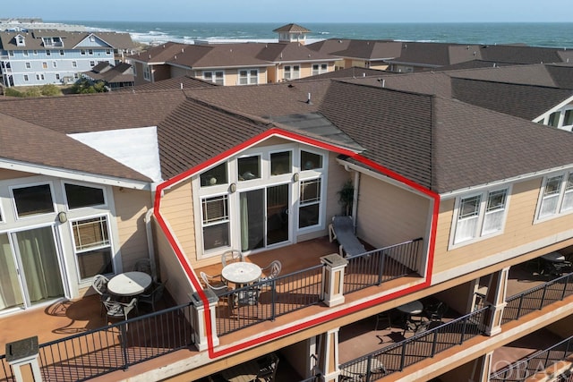 rear view of property featuring roof with shingles, a water view, and a balcony