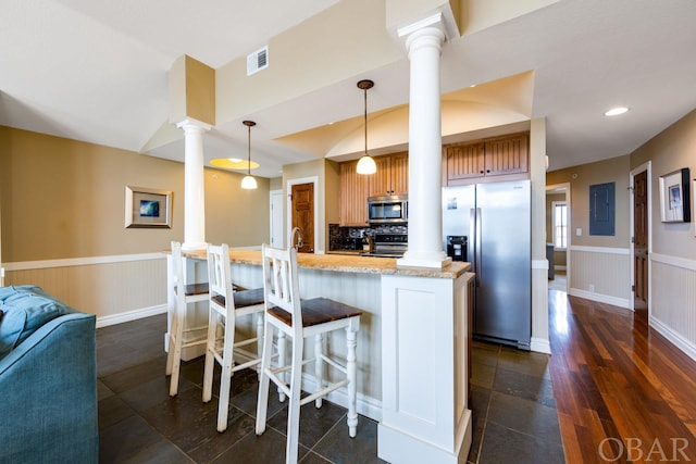 kitchen featuring a breakfast bar area, a wainscoted wall, stainless steel appliances, decorative light fixtures, and ornate columns