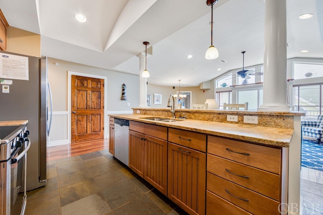 kitchen with pendant lighting, a wainscoted wall, appliances with stainless steel finishes, a sink, and light stone countertops