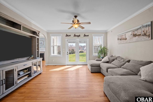 living area with ornamental molding, light wood-style flooring, baseboards, and a ceiling fan