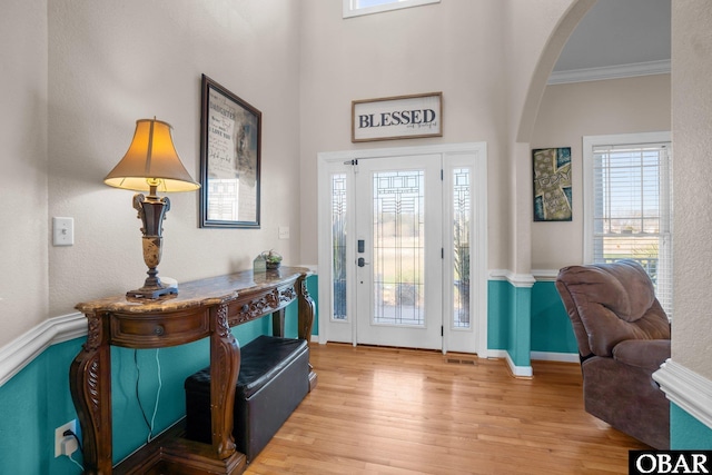 entryway with baseboards, visible vents, arched walkways, wood finished floors, and crown molding