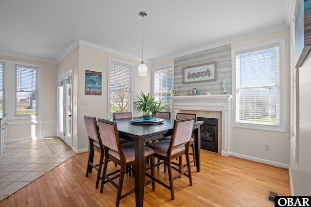 dining area with ornamental molding, light wood-type flooring, a tile fireplace, and baseboards