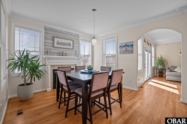 dining space with arched walkways, visible vents, ornamental molding, light wood-type flooring, and baseboards