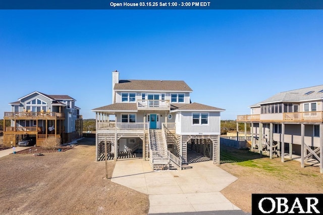 view of front of house featuring roof with shingles, a chimney, a balcony, a carport, and driveway