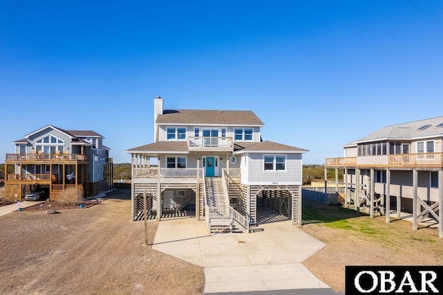 view of front of property featuring a shingled roof, concrete driveway, a chimney, a balcony, and a carport