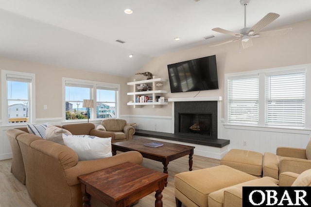 living room with a wainscoted wall, visible vents, a fireplace with raised hearth, light wood-style floors, and lofted ceiling