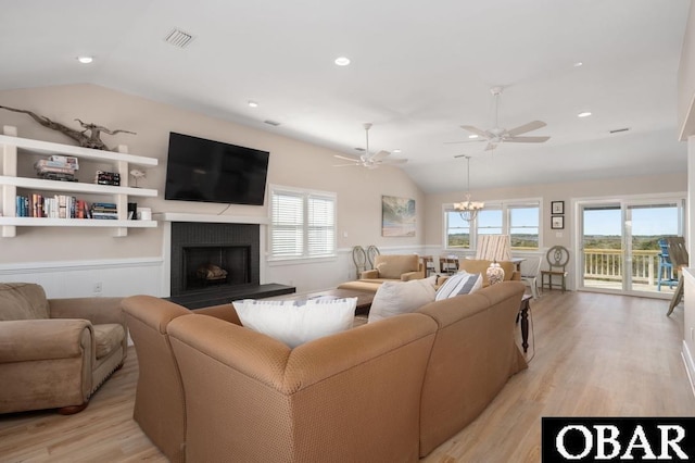 living area featuring light wood finished floors, visible vents, a fireplace with raised hearth, and lofted ceiling