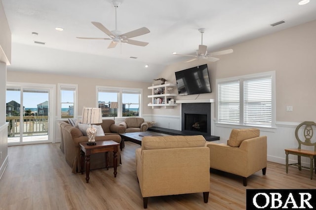 living area featuring visible vents, a fireplace with raised hearth, ceiling fan, light wood-style floors, and wainscoting