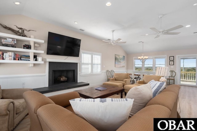 living area with plenty of natural light, a fireplace with raised hearth, wood finished floors, and vaulted ceiling